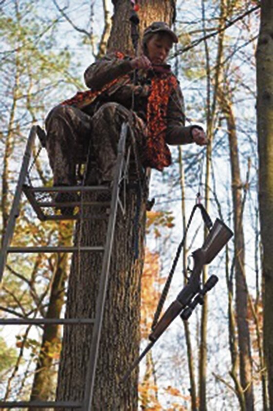 Hunter in tree stand with fall-arrest system and all other safety tools equipped